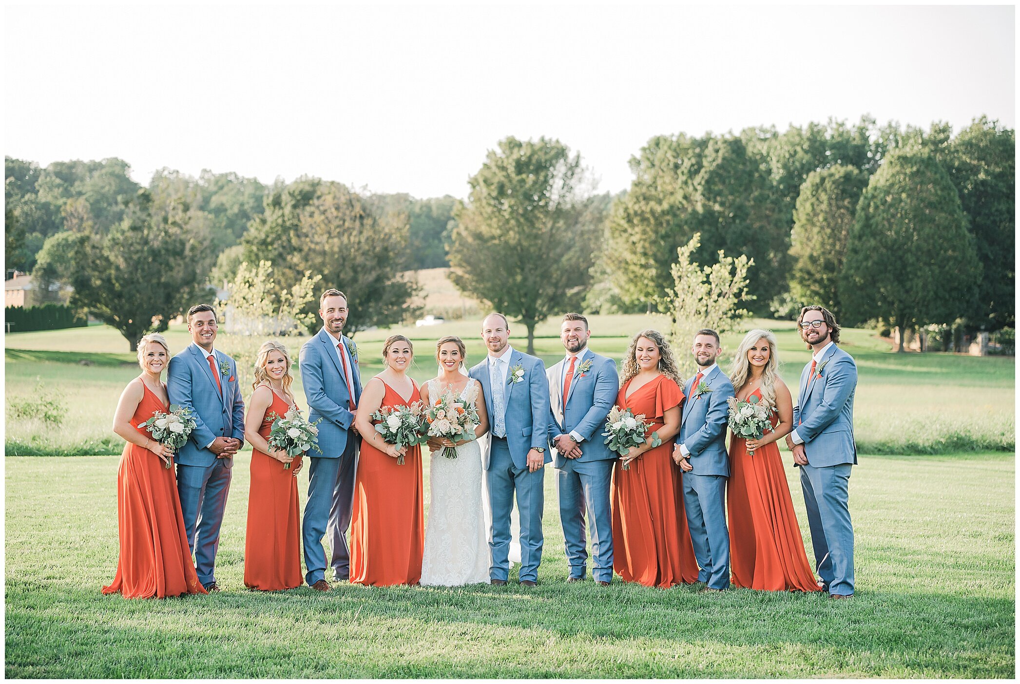 bridesmaids in orange gowns and groomsmen in navy suits pose at Granary at Valley Pike
