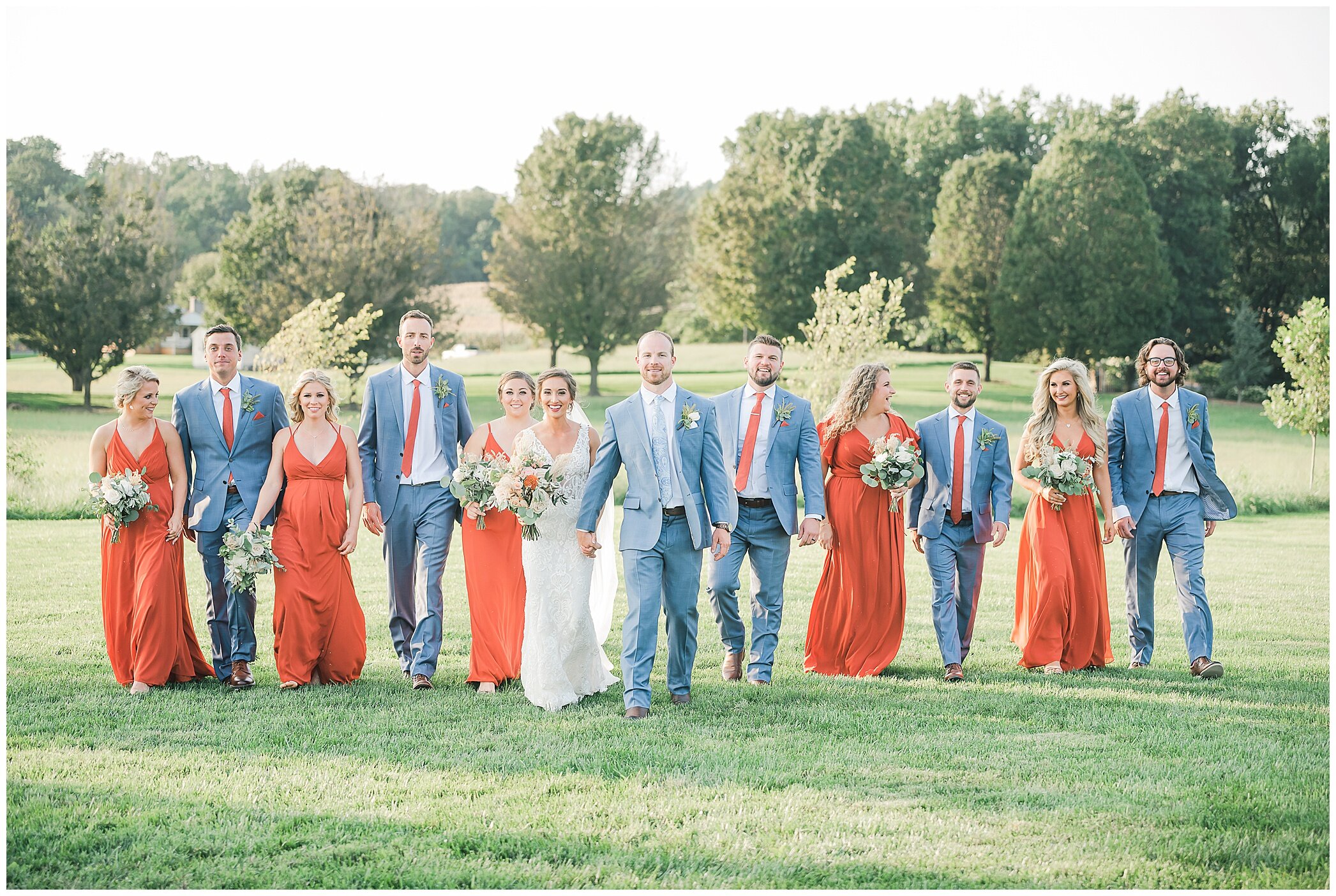 bridal party in navy blue and orange walks with bride and groom