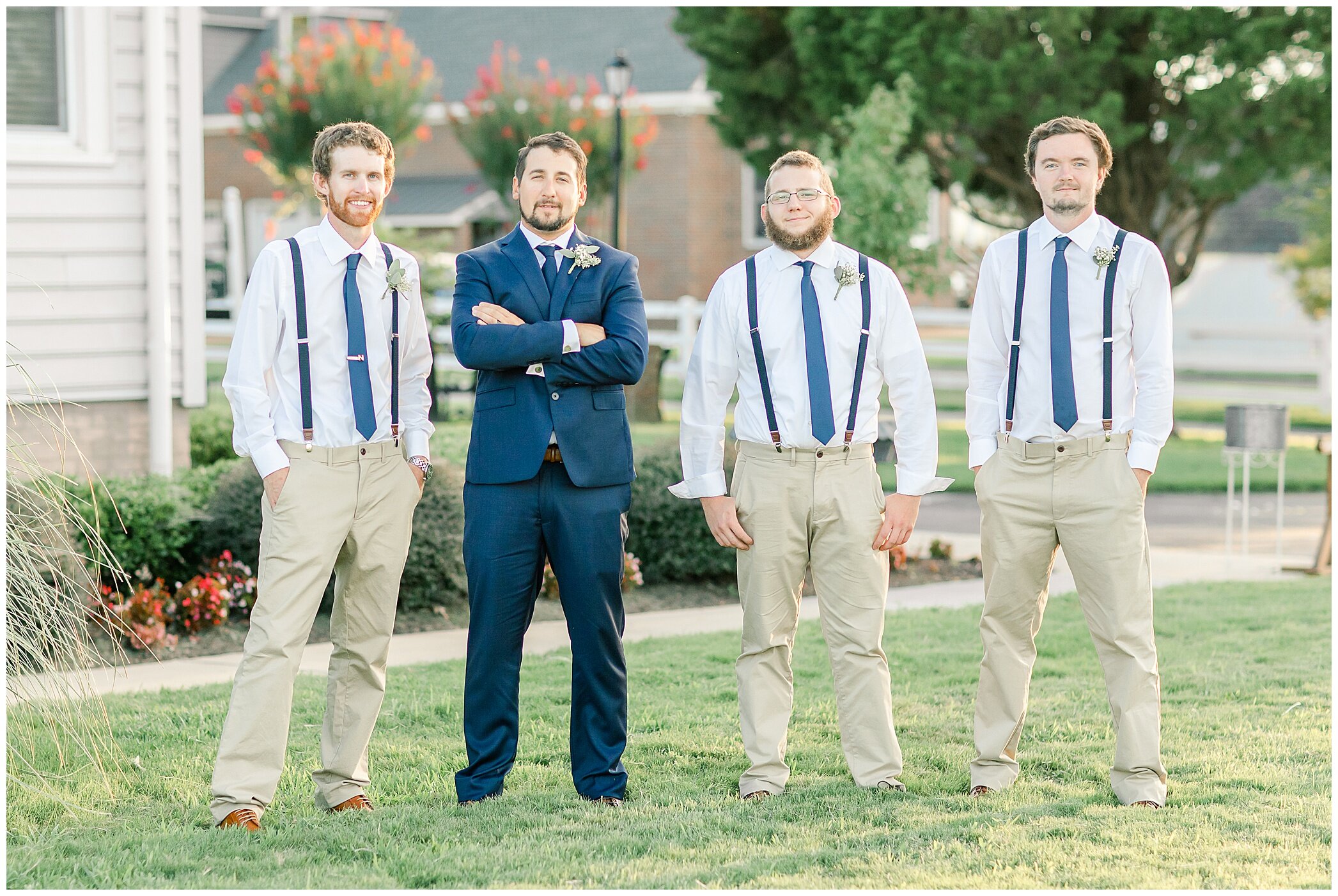 groom in navy suit poses with groomsmen in suspenders and khakis