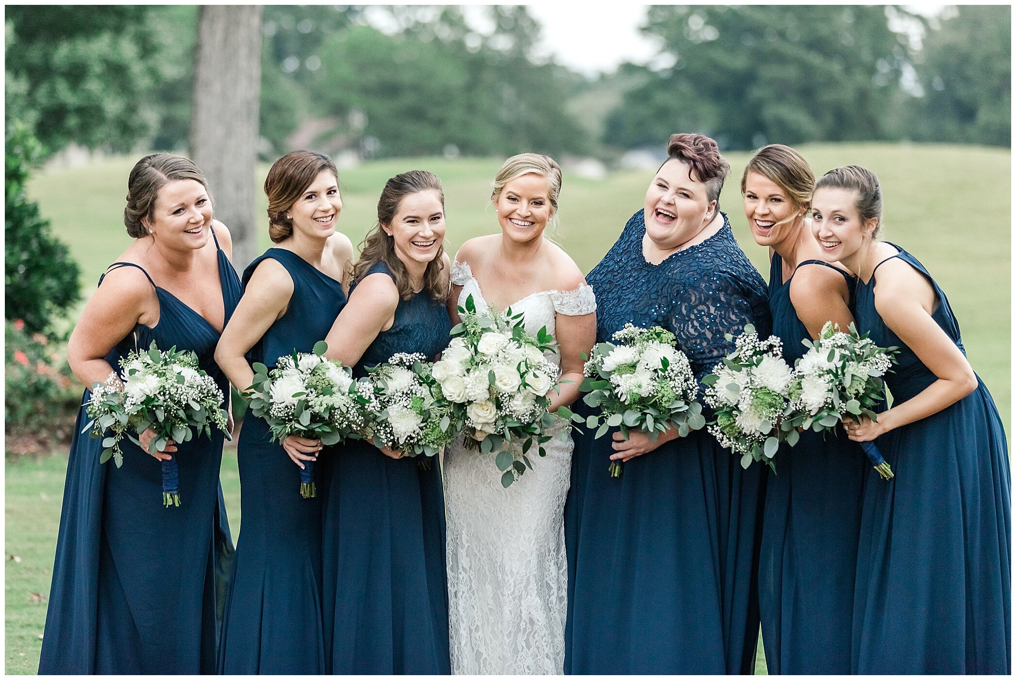 bridesmaids in navy gowns hold bouquets of white flowers