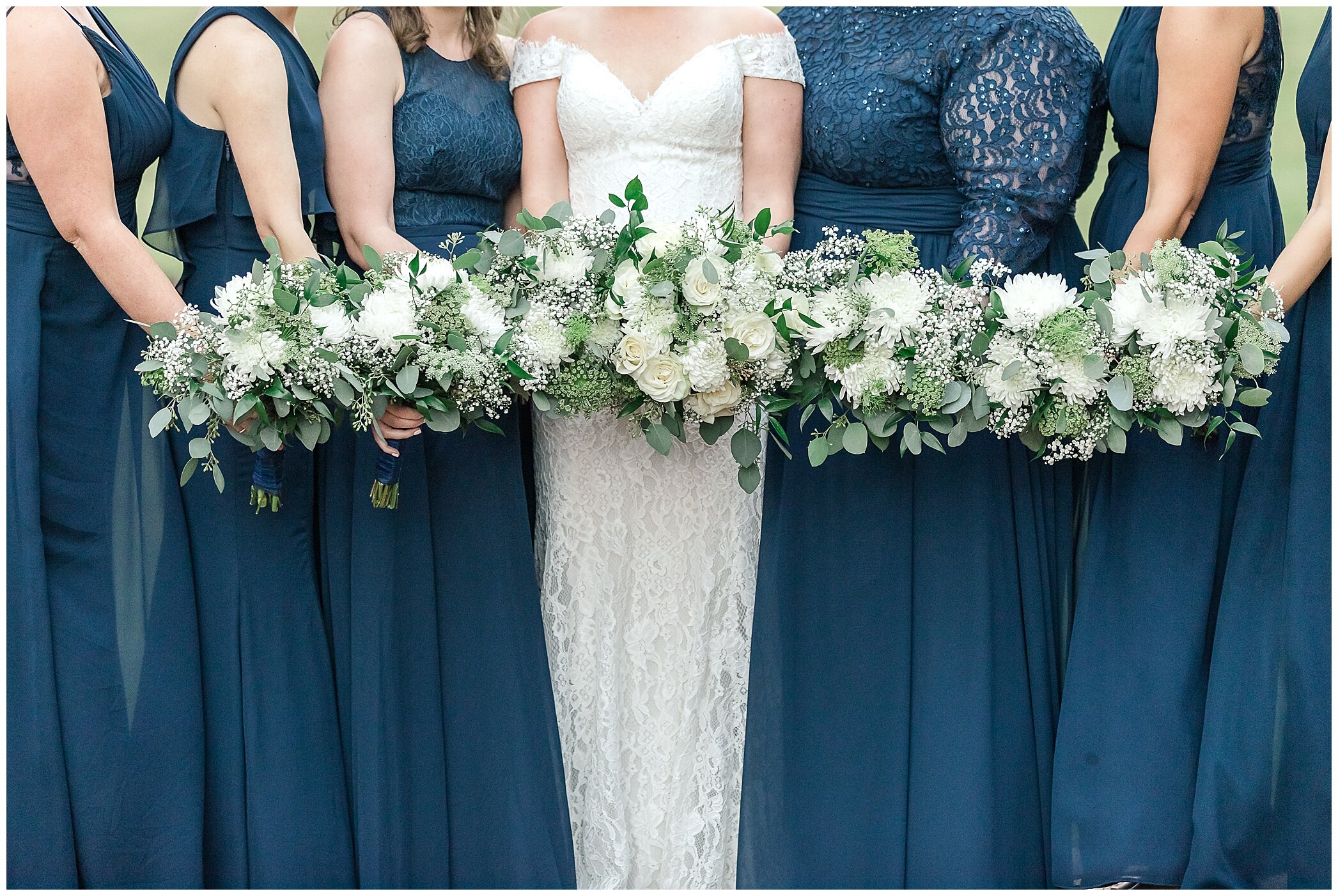 bridesmaids with ivory flowers and navy gowns pose with bride