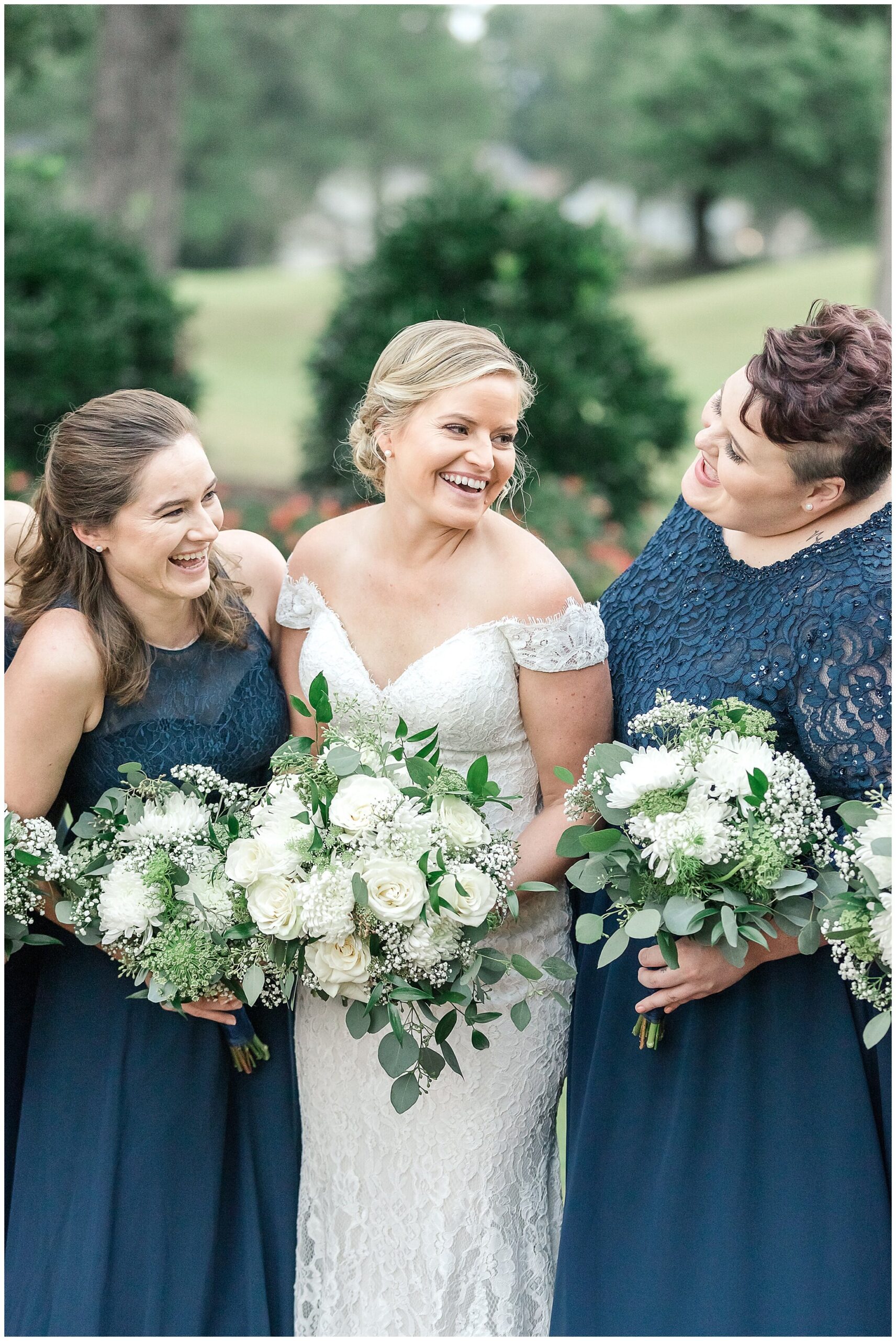bride holds bouquet with bridesmaids in navy gowns