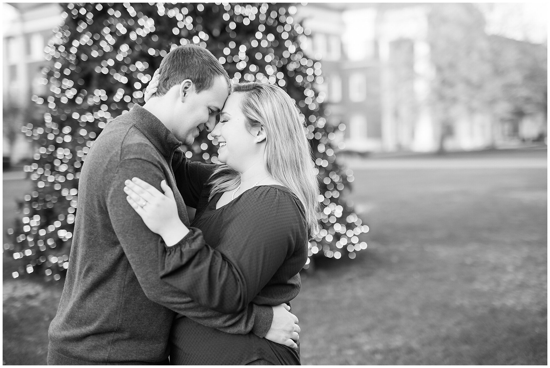 engaged couple stands nose to nose by Christmas tree at Christopher Newport University